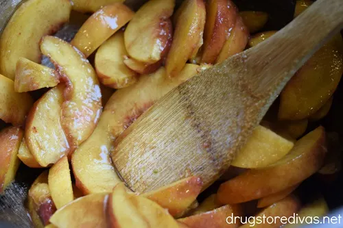 Marinated peach slices being stirred by a bamboo spoon.
