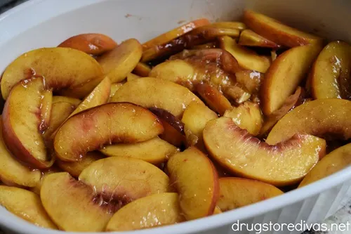 Marinated peach slices in the bottom of a white casserole pan.