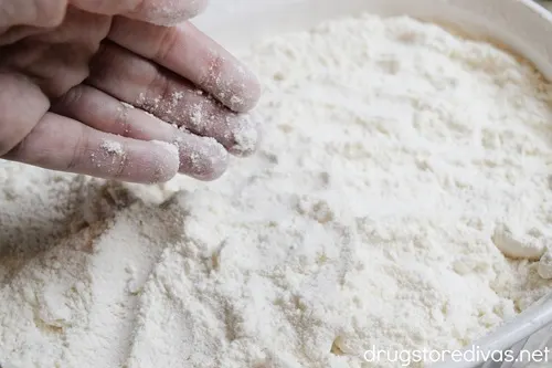 A hand putting white cake mix into a white casserole pan.