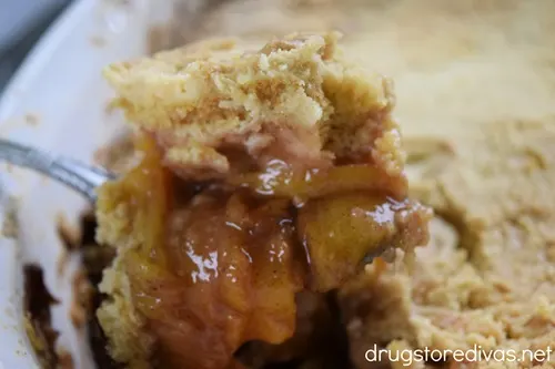 A large spoonful of peach cobbler above a pan of it.