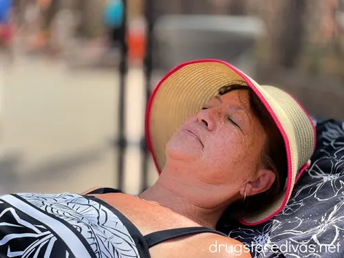 A woman in a black and white bathing suit laying down while wearing a straw hat.