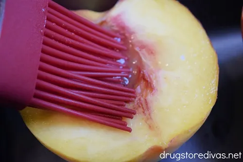 A pastry brush brushing butter on a peach half.