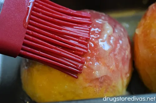 A pastry brush brushing butter on a peach half.