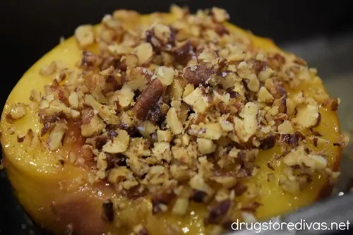 A peach half with chopped pecans on top.