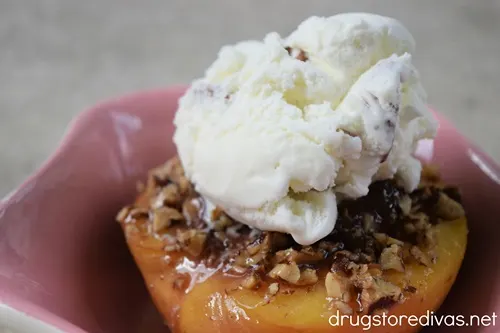 A baked peach with pecans and ice cream on top in a pink bowl.