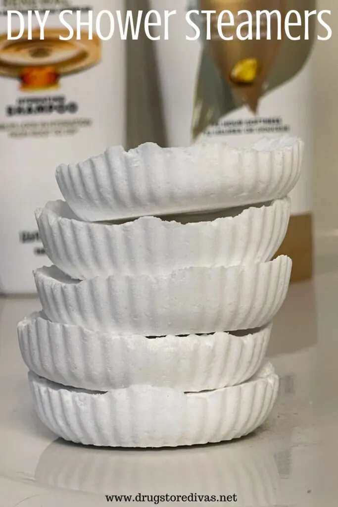 Five white shower steamers on a shelf with shampoo bottles behind them and the words "DIY Shower Steamers" digitally written above them.