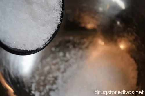 Epsom salt in a measuring cup being poured into a silver bowl.