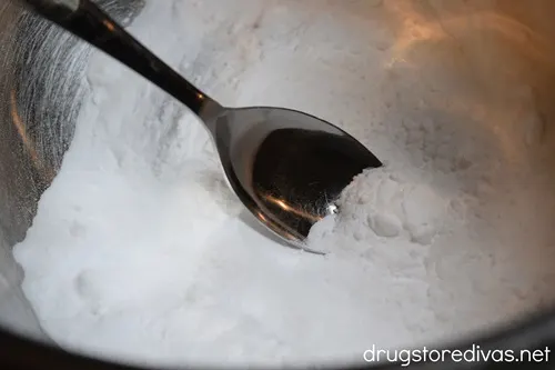 A spoon stirring a white powder that looks like salt in a silver bowl.