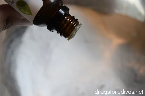 A bottle of essential oil above white powder in a silver bowl.