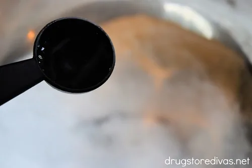 A black measuring spoon filled with liquid of above white powder in a silver bowl.