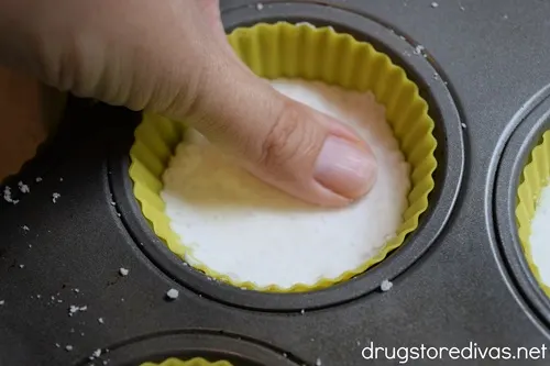 A thump pushing down white powder into a yellow silicone liner in a muffin tin.