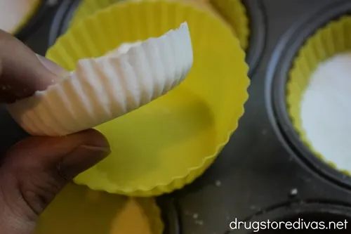 A hand holding a shower steamer above a cupcake pan with an empty yellow silicone liner.