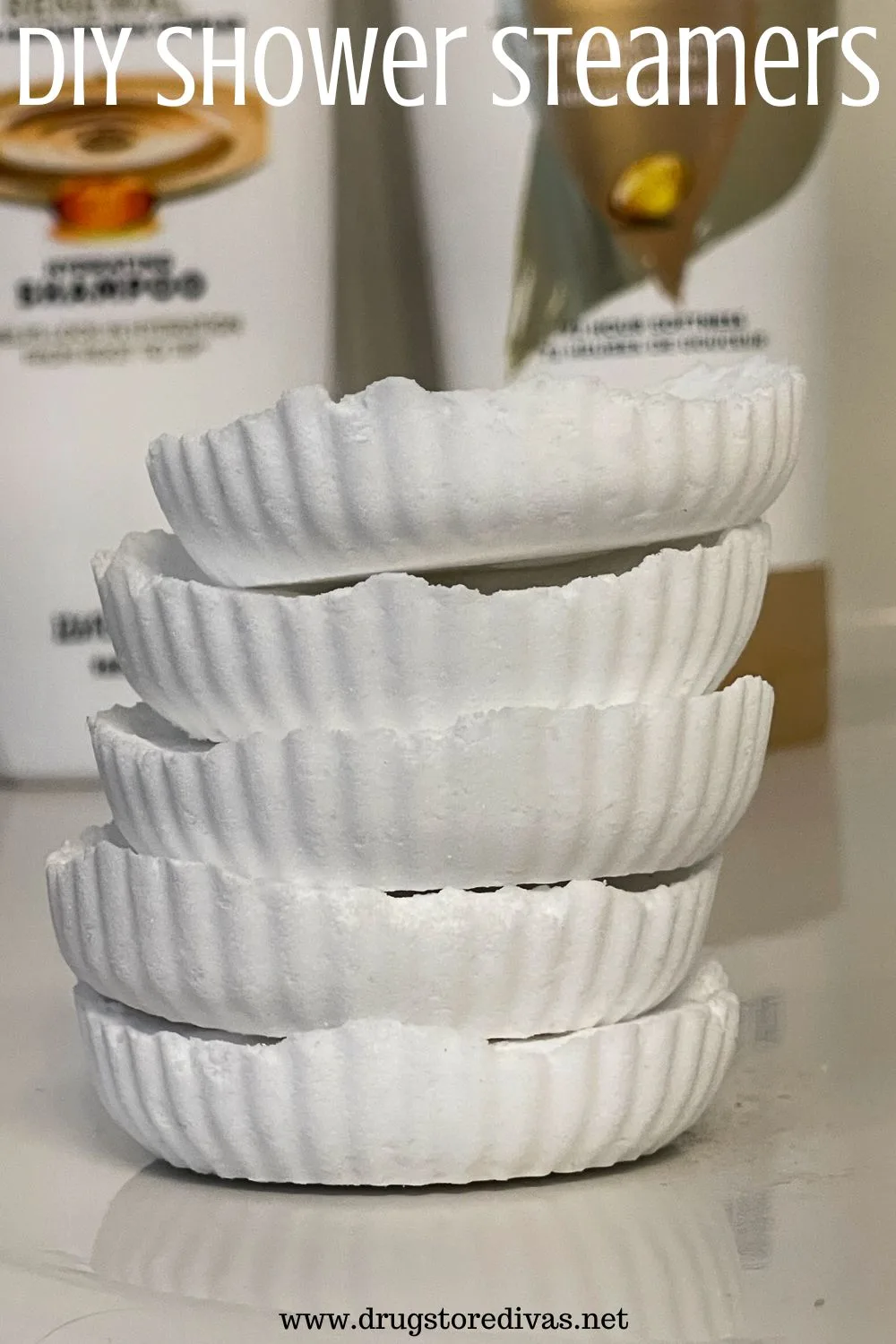 Five white shower steamers on a shelf with shampoo bottles behind them and the words 