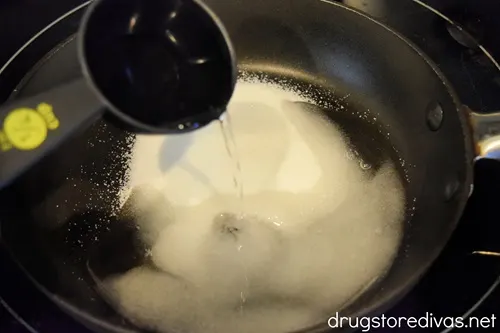Water in a measuring cup being poured into a pot with sugar in it.