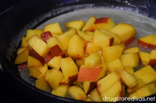 Cubed peaches in the middle of liquid sugar in a pan.
