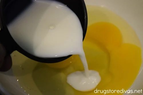 A measuring cup with milk being poured into a bowl of cracked eggs.