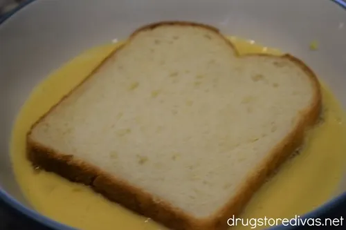 A piece of bread in an egg mixture in a blue bowl.