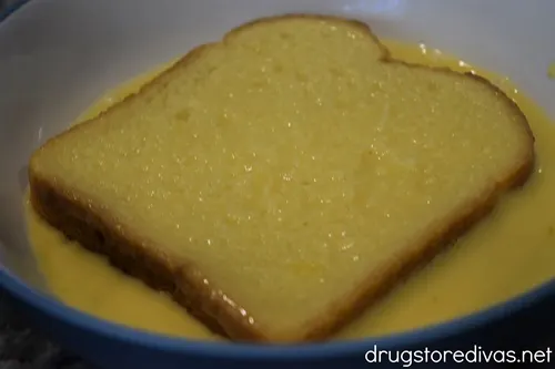 A piece of bread in an egg mixture in a blue bowl.