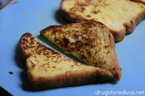 A piece of French toast cut in half on a blue cutting board.