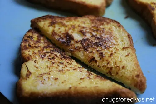 A piece of French toast cut in half on a blue cutting board.