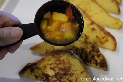 A measuring cup filled with peaches and peach juice above triangles of French toast.