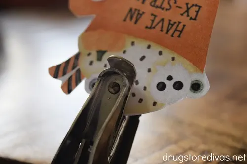 A single hole punch punching a hole in a paper cup that says "Have An Ex-Straw Special Halloween".