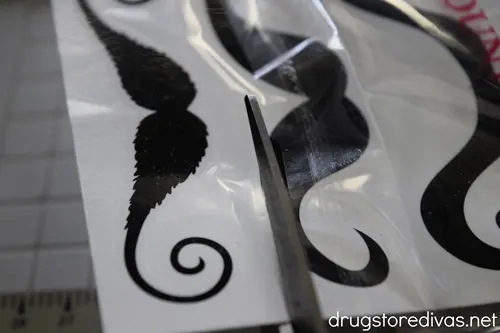 Scissors cutting a strip of mustache tattoos.