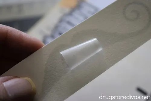 Fingers holding a rectangle piece of paper with a rolled piece of tape on it.