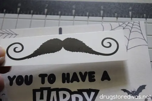 A mustache tattoo being stuck onto a Halloween card.