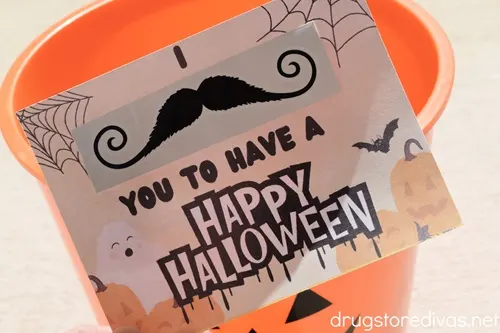 A Halloween card that says "I mustache you to have a Happy Halloween" where the mustache is a temporary tattoo going into a Halloween pumpkin bucket.