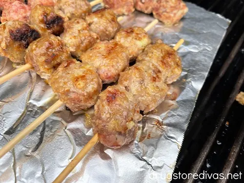 Cooked Meatball skewers on a piece of foil on a grill.
