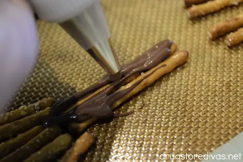 A piping bag putting chocolate on pretzel sticks.
