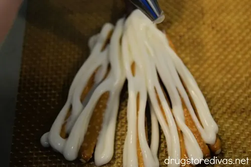 A piping bag putting white chocolate on pretzel sticks in a v-shape.