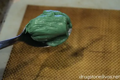 A spoon filled with melted green candy melts over a tray.