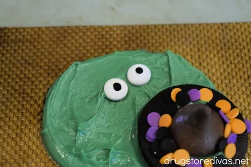 An Oreo cookie that looks like a hat and two candy eyeballs in a circle of melted green chocolate.