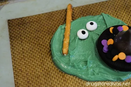 An Oreo cookie that looks like a hat, two candy eyeballs, and a pretzel stick in a circle of melted green chocolate.
