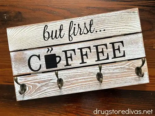 A wooden coffee cup holder than says "but first coffee" on it.