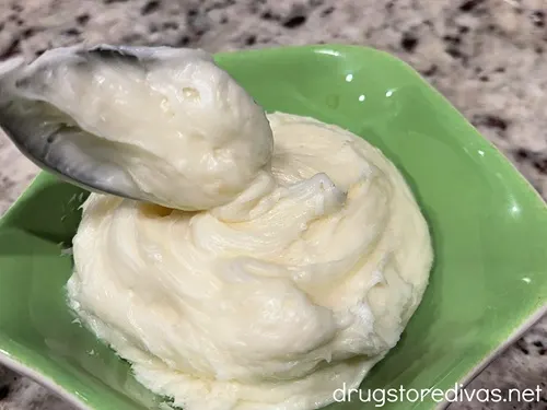 A spoon putting white frosting into a green bowl.