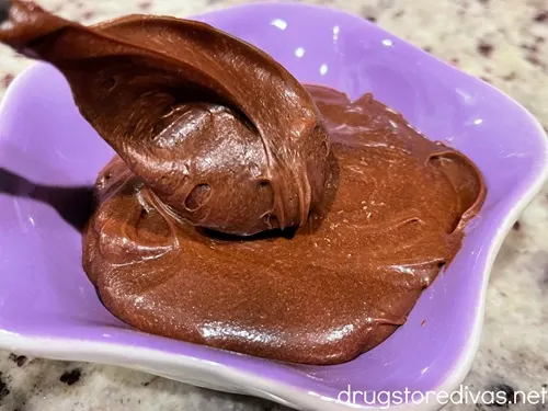 A spoon putting chocolate frosting into a purple bowl.