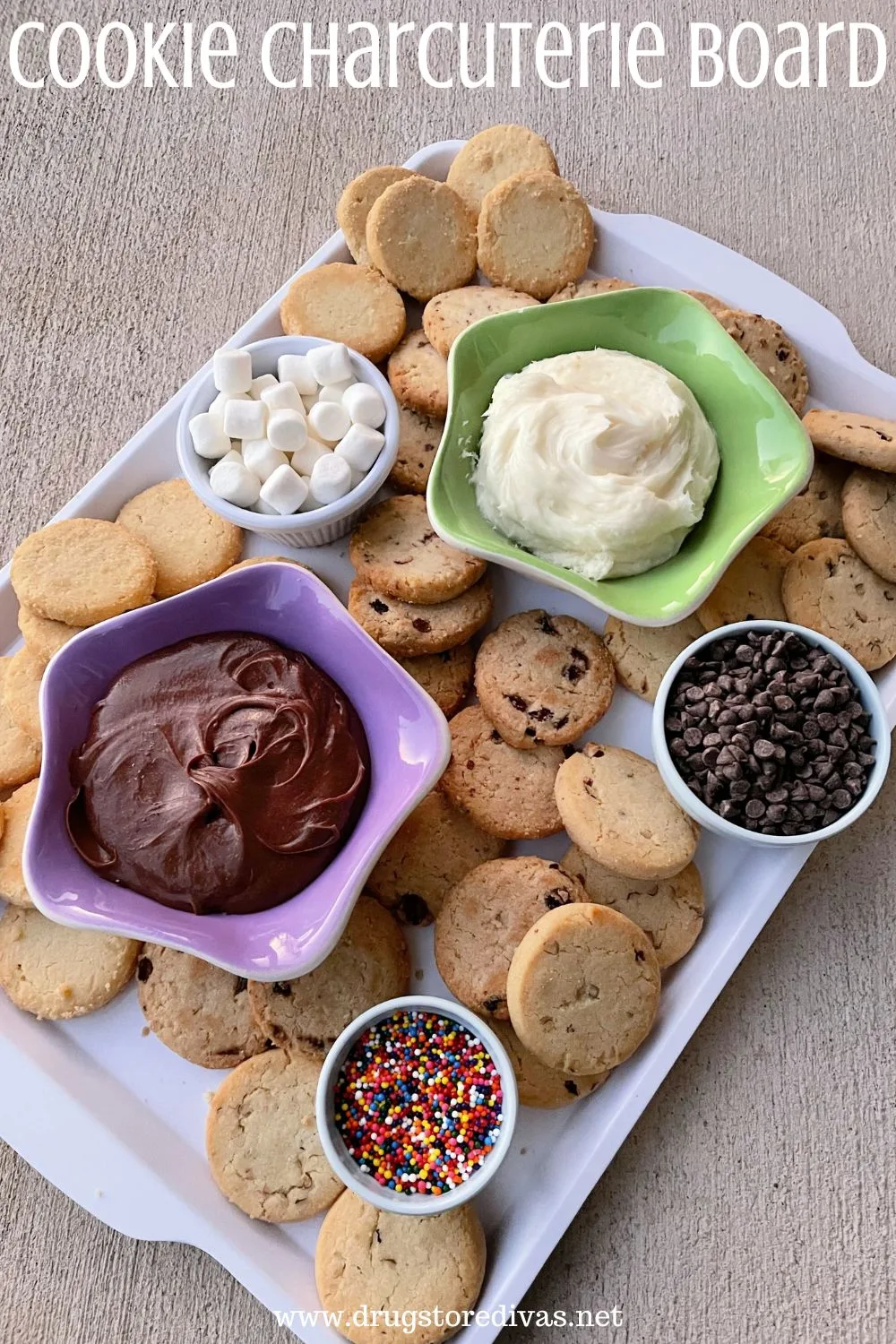 A white tray filled with cookies and bowls with chocolate icing, white icing, mini marshmallows, mini chocolate chips, and sprinkles with the words 