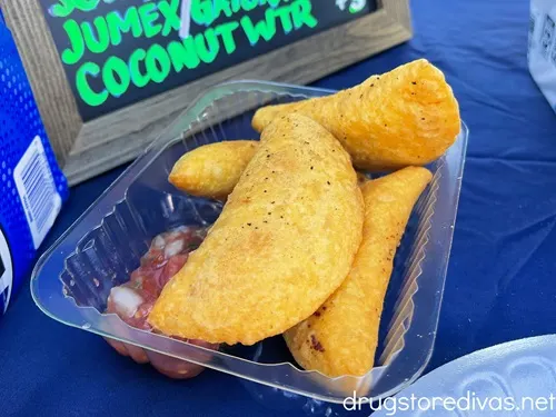 A plastic container with four empanadas and salsa on a blue tablecloth.