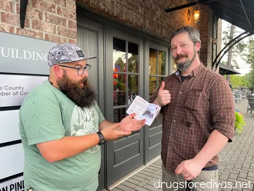 Two men standing outside of doors, which lead to Southern Pines Growler Company, holding an open passport.