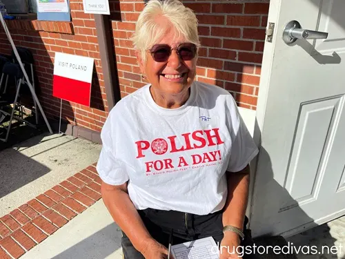 An older woman with sunglasses sitting in a chair wearing a shirt that says Polish For A Day.