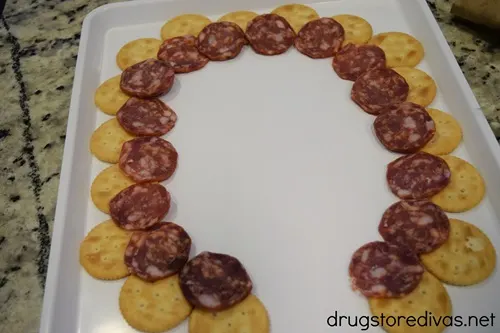 A semi circle of Ritz crackers and a semi circle of salami on a white tray.