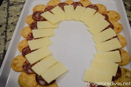 A semi circle of Ritz crackers, a semi circle of salami, and a semi circle of cheese on a white tray.
