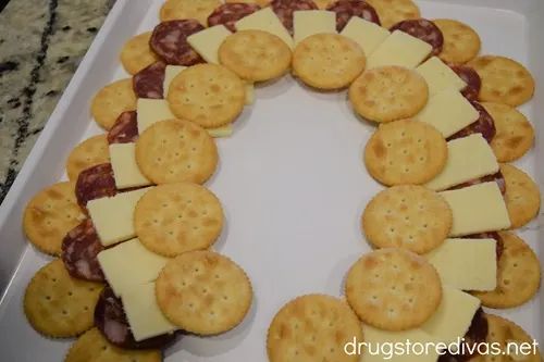 A semi circle of Ritz crackers, a semi circle of salami, a semi circle of cheese, and another semi circle of Ritz crackers on a white tray.