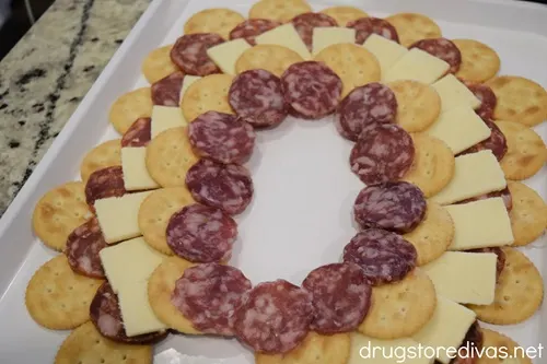 A semi circle of Ritz crackers, a semi circle of salami, a semi circle of cheese, and another semi circle of Ritz crackers and another semi circle of salami on a white tray.
