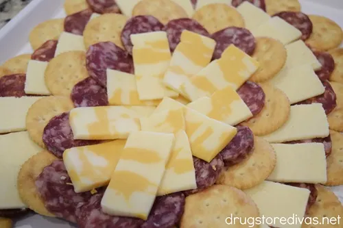 A semi circle of Ritz crackers, a semi circle of salami, a semi circle of cheese, and another semi circle of Ritz crackers and another semi circle of salami, and a bunch of cheese slices in the middle on a white tray.