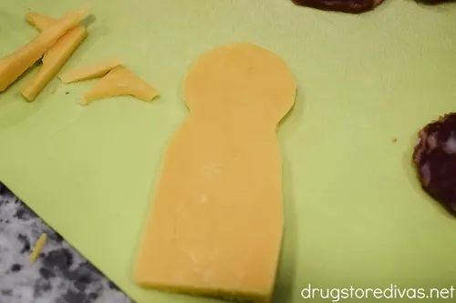 Cheddar cheese that looks like a body on a green cutting board.