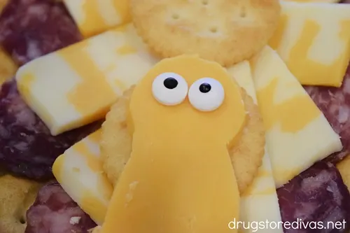 A cheese slice that looks like a body with two candy eyes on top of cheese and crackers.